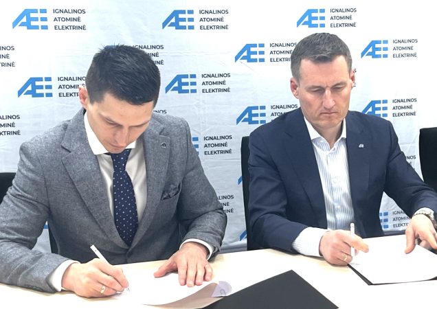 Du vyrai pasirašo sutartį Ignalinos atominės elektrinės fone, dėvi kostiumus, fonas su AE logotipais.