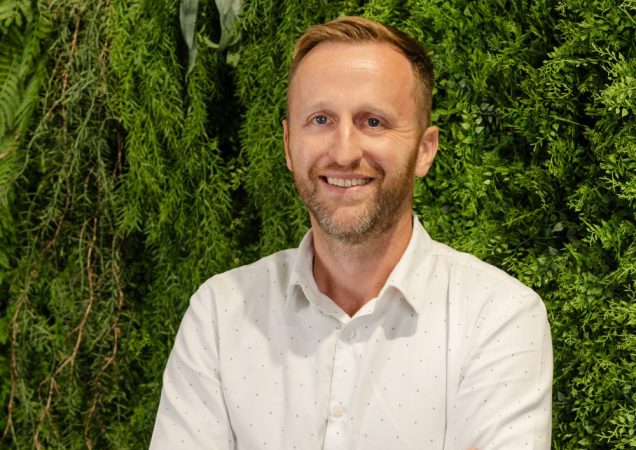 Karolis Sankovski stovi prie žalios spalvos sienelės