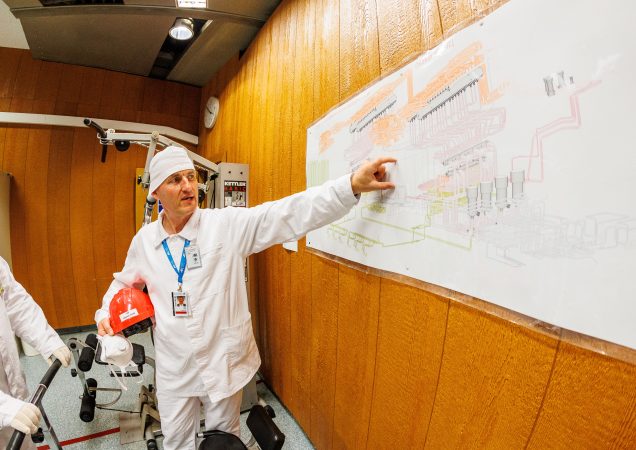 Darbuotojas su apsauginiais rūbais rodo į schemą ant sienos Ignalinos atominėje elektrinėje.