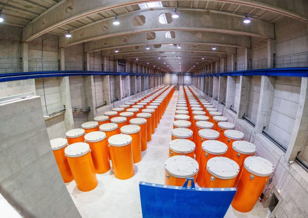 Ilga betoninė saugykla su eilėmis oranžinių konteinerių, skirtų radioaktyvioms atliekoms laikyti.