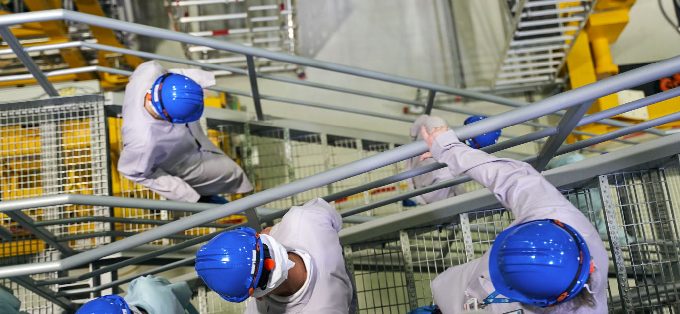 Ignalinos atominės elektrinės darbuotojai su apsauginiais šalmais leidžiasi metaliniais laiptais.