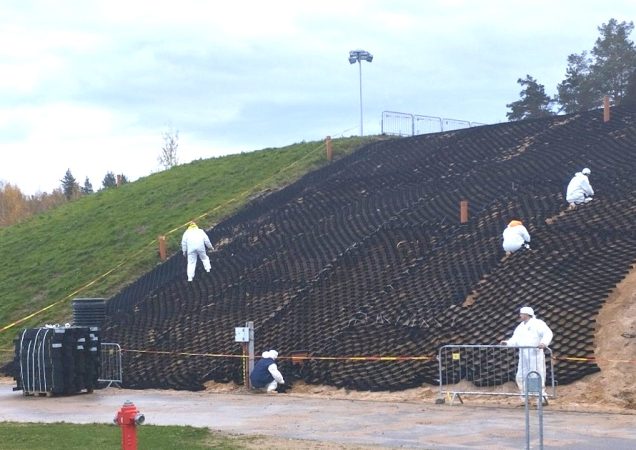 Darbuotojai apsauginiais kombinezonais montuoja šlaito sutvirtinimo sistemą.