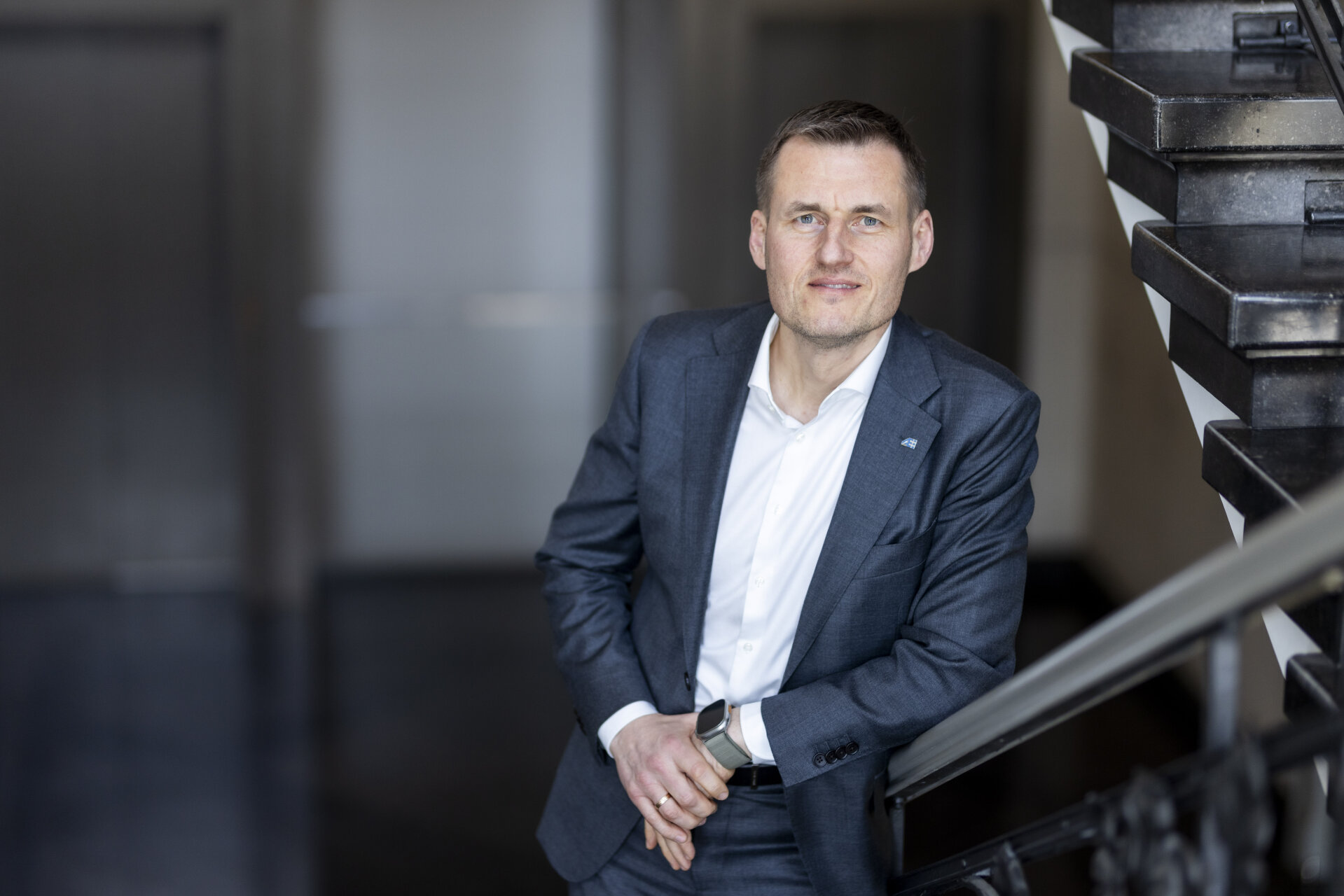 Įmonės vadovas pozuoja oficialioje aplinkoje, vilkėdamas kostiumą