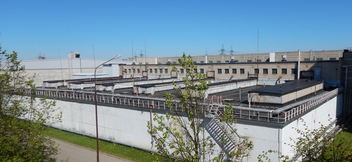 Ignalinos atominės elektrinės pastatas su techninėmis konstrukcijomis ir išorinėmis kopėčiomis.
