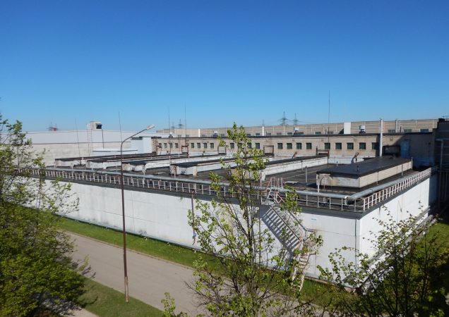 Ignalinos atominės elektrinės pastatas su techninėmis konstrukcijomis ir išorinėmis kopėčiomis.