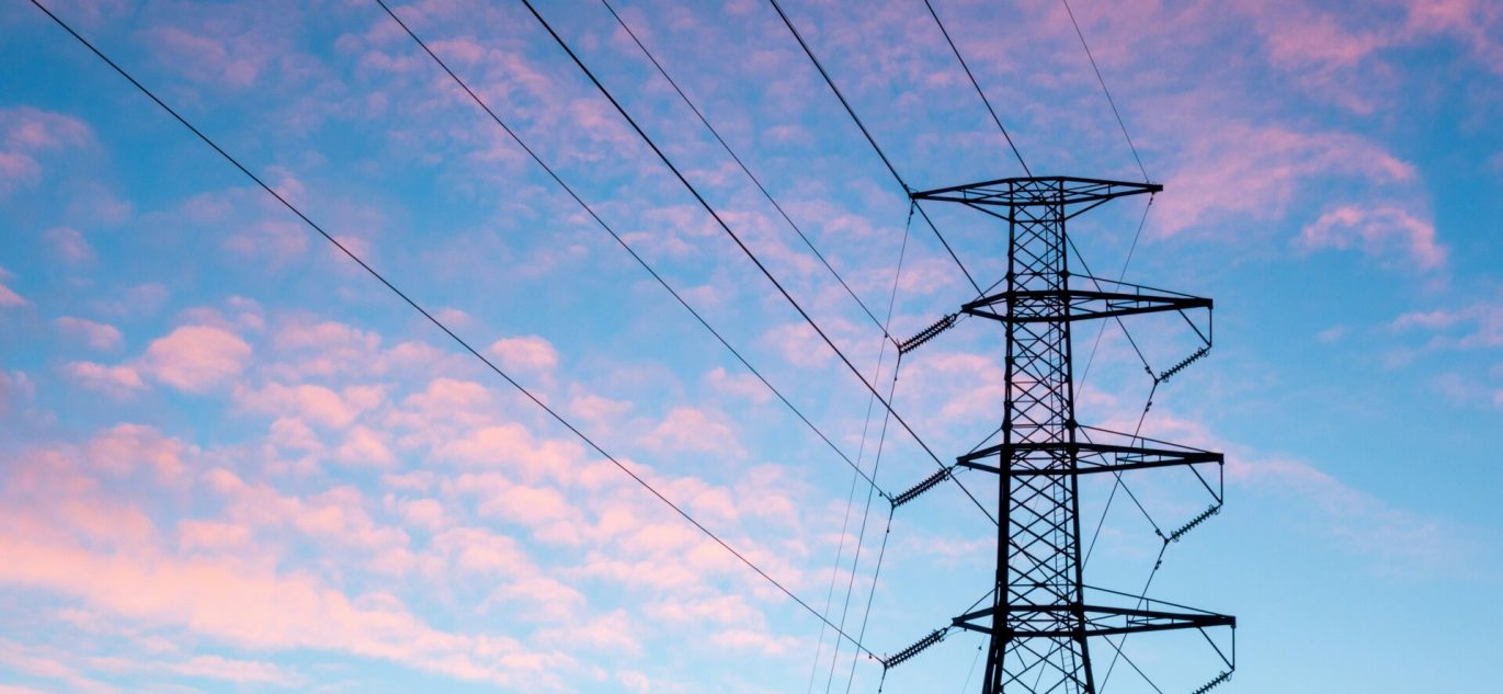 Elektros perdavimo linijos bokštas su laidais priešais rausvai mėlyną vakaro dangų.