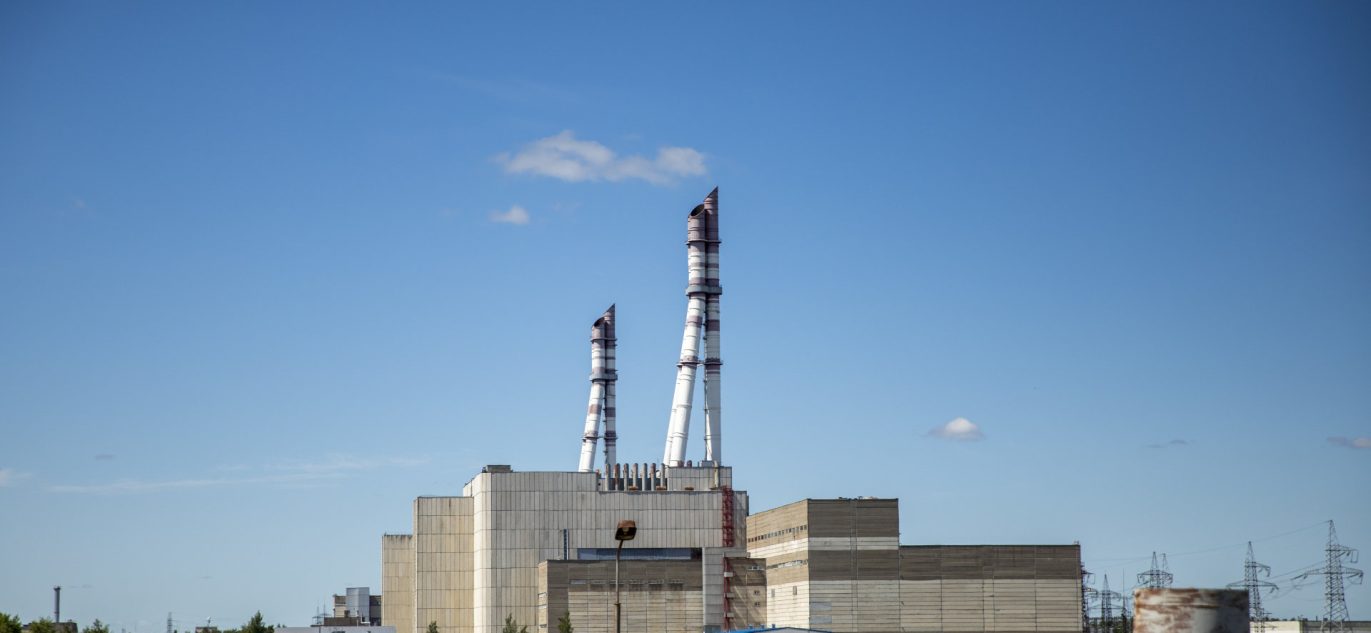Ignalinos atominės elektrinės pastatų kompleksas su dviem aukštais kaminų, fotografuotas giedrą dieną.