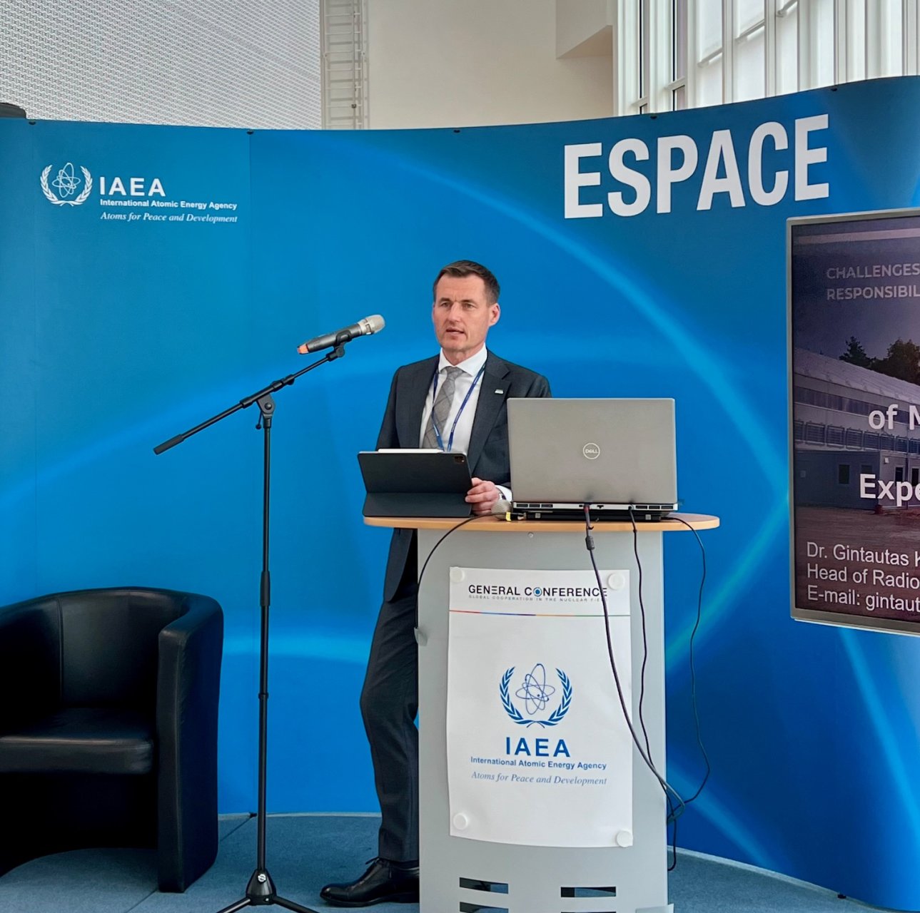 Pristato radioaktyviųjų atliekų saugyklos projektą IAEA generalinėje konferencijoje, stovėdamas prie tribūnos su nešiojamuoju kompiuteriu ir mikrofonu, fone – IAEA logotipas ir mėlynas stendas su užrašu „ESPACE“