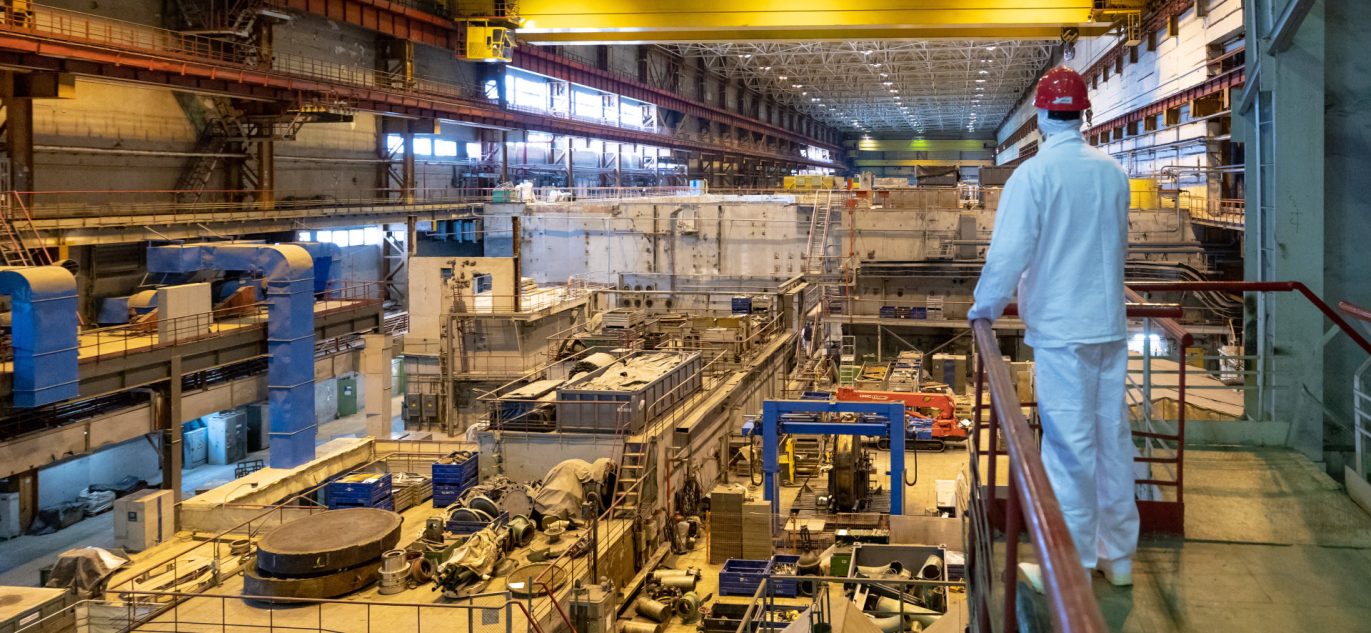 Ignalinos atominės elektrinės vidus – darbuotojas apsauginiuose rūbuose stebi reaktoriaus salę su įranga.