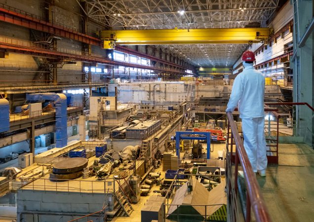 Ignalinos atominės elektrinės vidus – darbuotojas apsauginiuose rūbuose stebi reaktoriaus salę su įranga.