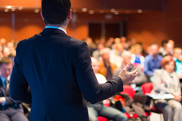 Vyras kostiumu skaito pranešimą konferencijoje auditorijai.