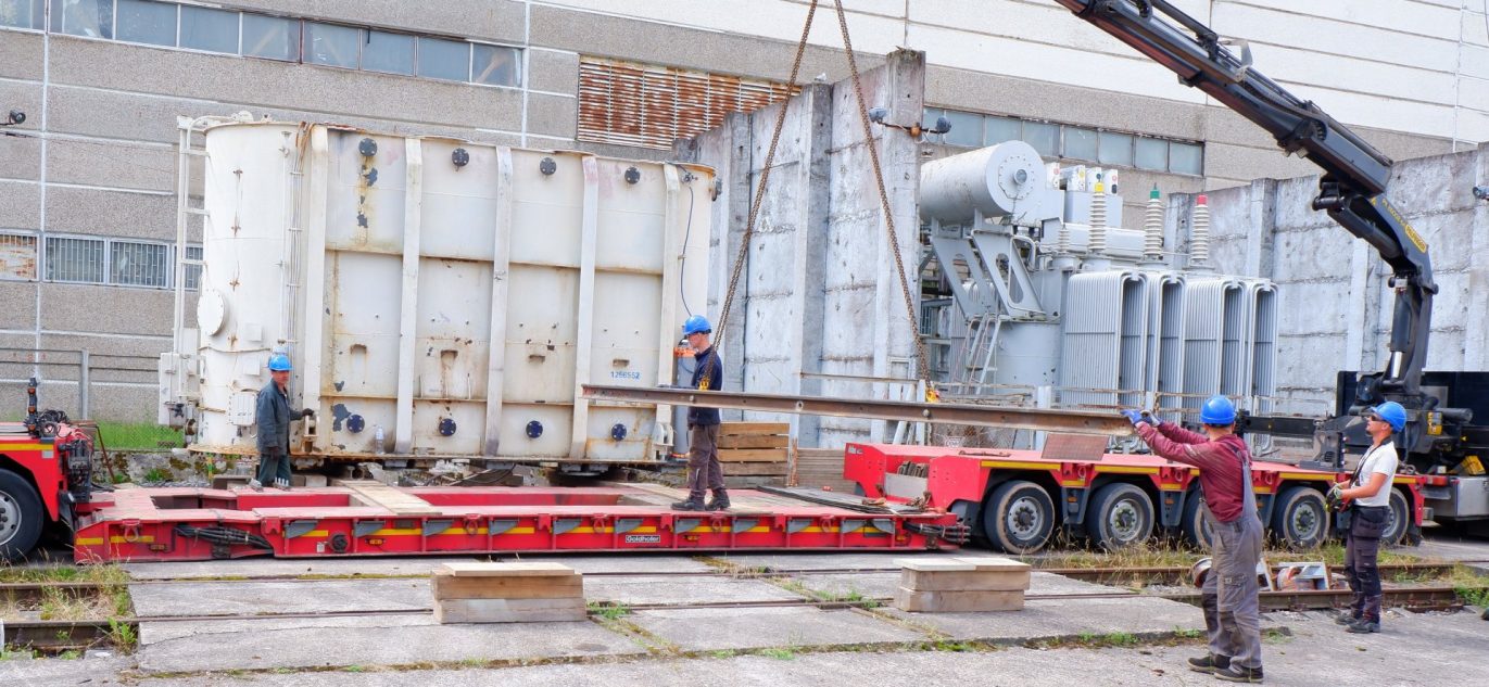 Darbininkai ruošia transformatorių kėlimui ant specialios transportavimo platformos prie Ignalinos atominės elektrinės pastato.