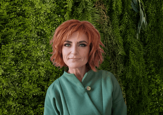 Aurelija Baronienė stovi prie žalios spalvos sienelės