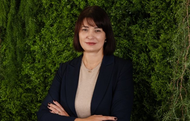 Olga Lakina-Raubė stovi prie žalios spalvos sienelės