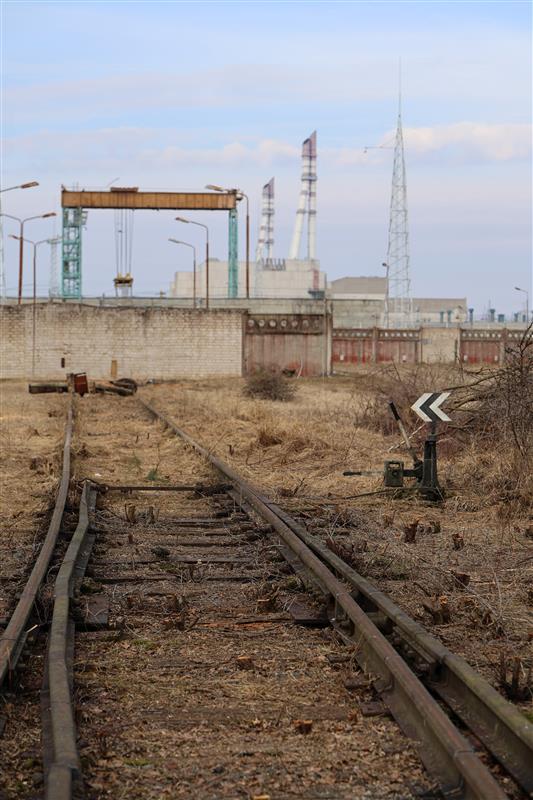 Ignalinos atominės elektrinės Laikinosios panaudoto branduolinio kuro saugyklos teritorijos teritorija, matomi seni traukinio bėgiai, fone - atominė elektrinė